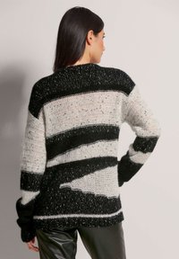 Strickpullover mit horizontalen schwarz-weißen und grauen Streifen, der eine lockere Passform und einen strukturierten, flauschigen Stoff mit weitem Ausschnitt präsentiert.