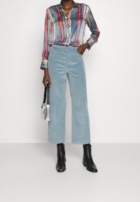 Gestreiftes, mehrfarbiges Hemd mit langen Ärmeln; hellblaue Cord-Hosen mit weitem Bein und vorderen Knöpfen; schwarze Stiefeletten; silberne Tasche.