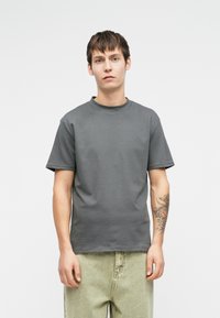 Γκρίζο βαμβακερό t-shirt με στρογγυλή λαιμόκοψη και κοντά μανίκια. Το ύφασμα έχει λεία υφή. Διαθέτει άνετη εφαρμογή και απλό σχέδιο.