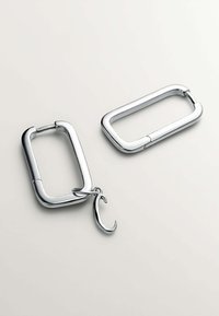 Llavero de metal plateado con forma ovalada, que cuenta con un gancho de sujeción y un acabado liso y brillante. Se muestran dos piezas una al lado de la otra.