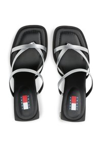 Sandalias negras con una suela gruesa, con tiras cruzadas de color plateado. La plantilla tiene un logotipo con acentos en rojo, blanco y azul.