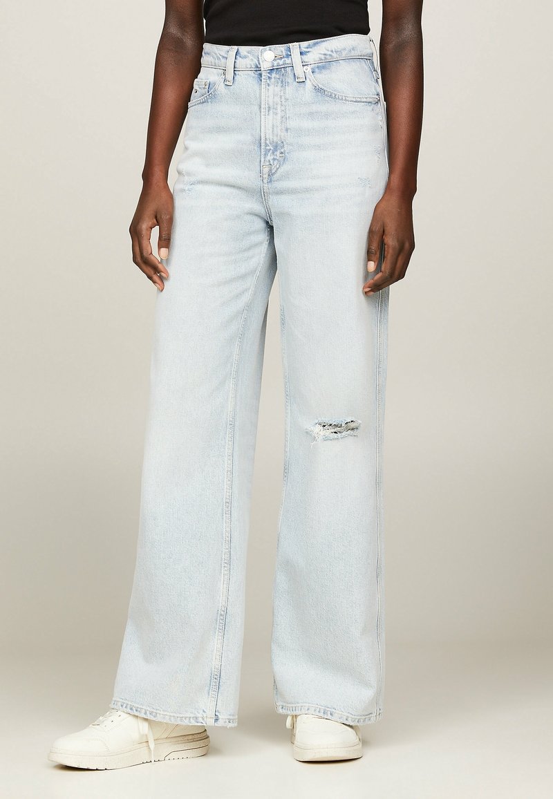 Jeans de mezclilla de pernera ancha en azul claro, con un patrón desgastado cerca de la rodilla, cintura alta y estilo clásico de cinco bolsillos.