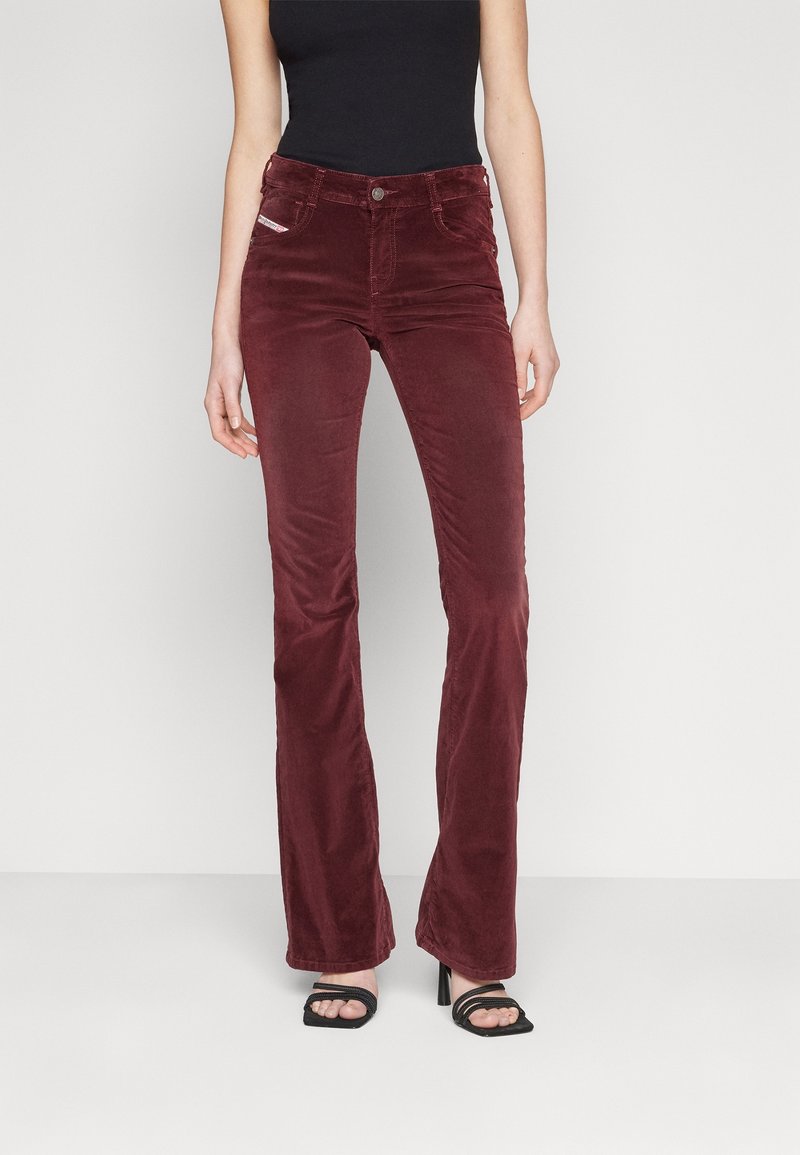Pantalones acampanados de pana burdeos con cierre de botón, bolsillos y un acabado texturizado, combinados con sandalias negras de tacón.