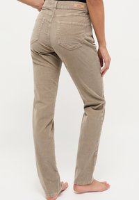 Beige corduroy broek met een rechte pijp, voorzien van twee achterzakken en een subtiele textuur. Merklabel zichtbaar boven de tailleband.