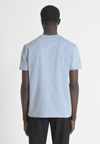 T-shirt a maniche corte blu chiaro con colletto tondo e texture liscia, vista da dietro. Design minimalista, senza motivi o dettagli visibili.