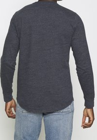 Dlouhý rukáv, tmavě šedá košile s zaobleným spodním lemem, vyrobená z texturované tkaniny; má fitted rukávy a kulatý výstřih.