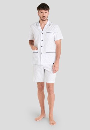 Conjunto de pijama corto blanco con lunares azules, que incluye una camiseta de manga corta, bolsillo en el pecho y ribete azul marino en el cuello y los pantalones cortos.