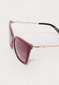 Rdeče in zelene plastične sončna očala s kvadratno obliko, gradientnimi lečami, kovinskimi ročaji z zlatim srčastim okrasom in graviranim imenom blagovne znamke.