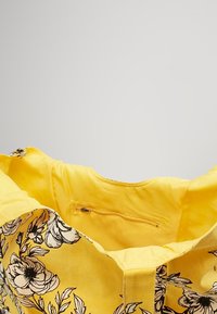 Borsa a tracolla gialla con stampa floreale nera, dotata di una tasca interna con zip. Il tessuto ha una consistenza piacevole. Design a apertura superiore.