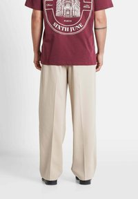 Burgundy cotton t-shirt with a graphic print and a beige wide-leg trouser, featuring a smooth texture and a tailored fit. Black shoes complete the look.