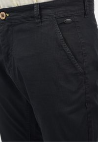 Pantalon en tissu noir avec un motif texturé subtil, doté d'une fermeture à bouton et de poches avant inclinées. Design élégant et droit.