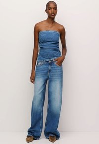 Denim tube top ima peplum rob; uparen s širokim izblijedjelim plavim trapericama. Smeđe cipele upotpunjuju outfit. Glatka tekstura i ležeran dizajn.