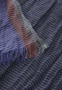 Woven textile featuring dark blue and purple stripes with fringed edges in reddish-brown and grey. Soft texture, lightweight, and layered appearance.