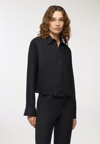 Camicia nera a maniche lunghe con bottoni, realizzata in un tessuto leggero e morbido, con una vestibilità rilassata e maniche con polsini. Nessun motivo o dettaglio visibile.