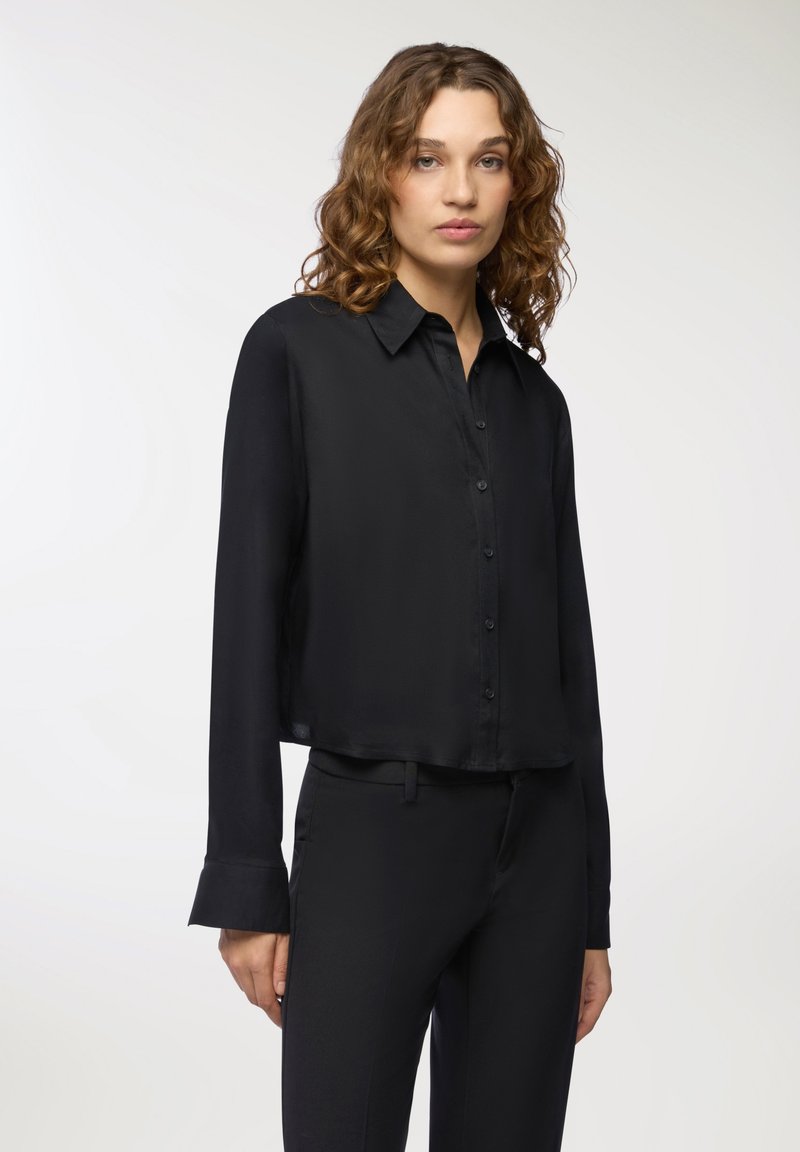 Camicia nera a maniche lunghe con bottoni, realizzata in un tessuto leggero e morbido, con una vestibilità rilassata e maniche con polsini. Nessun motivo o dettaglio visibile.