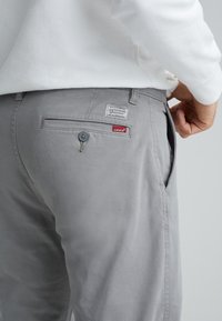 Szare spodnie z bawełny o gładkiej fakturze, z tylną kieszenią z guzikiem oraz metką Levi's na pasku.