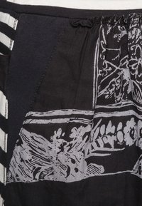 Musta kangas, jossa on monimutkaisia harmaita kukka- ja abstrakteja kuvioita. Sisältää tekstuuripinnan ja kerrotun vyötärön, jossa on hienovaraisia yksityiskohtia.