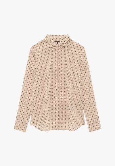 Blusa beige a maniche lunghe con pois rossi, colletto e dettaglio di nodo frontale, posata su uno sfondo bianco.