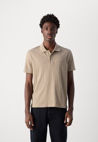 Polo beige in un tessuto morbido e texture, con collo a riviera, maniche corte e un discreto logo ricamato sul petto.