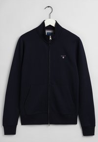 Felpa con zip di colore navy realizzata in un tessuto morbido, con colletto alto, due tasche frontali e un piccolo logo sul lato sinistro del petto.