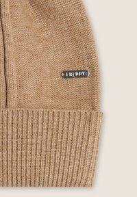 Cappello lavorato a maglia beige con risvolto a costine, dotato di un'etichetta metallica con il marchio "FREDDY". Tessuto morbido con una vestibilità leggermente ampia sulla parte superiore.