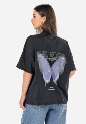 Svart oversized t-shirt med fjärilsillustration i blått och grått på baksidan, med texten: "VILA. Glöm aldrig att flyga." Tillverkad av bomull.