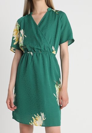 Robe portefeuille verte en tissu léger, ornée d'un motif floral sur l'ourlet et d'une surface texturée. Taille élastique pour un bon ajustement.