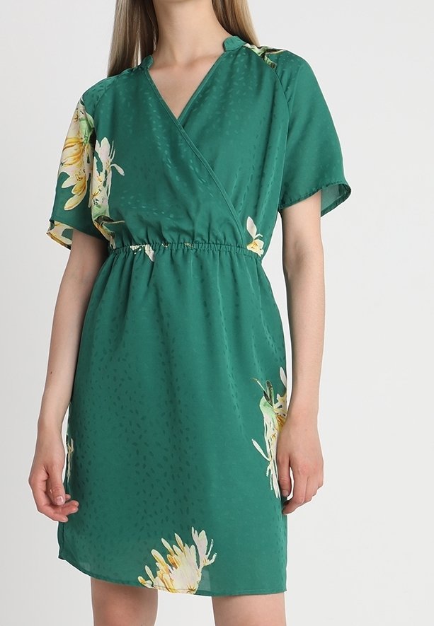 Robe portefeuille verte en tissu léger, ornée d'un motif floral sur l'ourlet et d'une surface texturée. Taille élastique pour un bon ajustement.