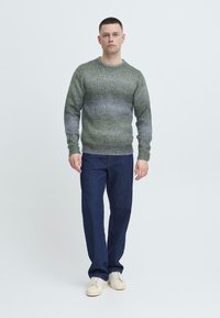 Grønn gradient strikkegenser med ribbestrikkede mansjetter og hem, paret med mørkeblå denimbukser og kremfargede sneakers. Enkelt, uformelt antrekk.
