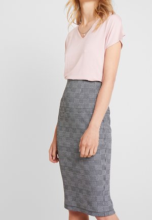 Vrouw draagt een lichtroze blouse met korte mouwen, ingestopt in een hoog getailleerde zwart-witte geruite kokerrok.