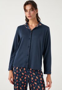 Set de pijamale bleumarin, cu bluza cu mânecă lungă și nasturi și pantaloni cu model de turturi și ornamente. Material moale, cu o croială lejeră.