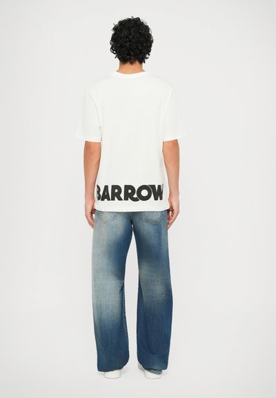 Camiseta blanca con gran texto negro "BARROW" en la parte posterior, combinada con jeans de denim azul de pierna ancha con un acabado desgastado.