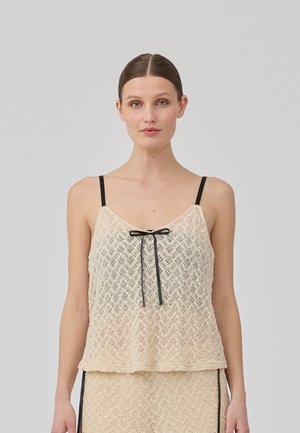 Peplum top made of light woven fabric, featuring a cream and beige color gradient, black straps, and a front ribbon tie detail.