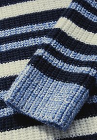Stickad tröja med horisontella ränder i marinblått, ljusblått och vitt. Mjuk textur med ribbade manschetter och en avslappnad passform.
