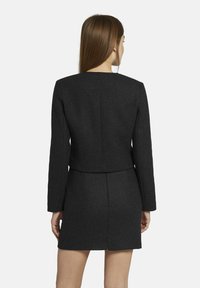 Zwarte wollen blend jas met lange mouwen en een cropped ontwerp, gecombineerd met een bijpassende strakke mini rok, met een gladde textuur en eenvoudige lijnen.