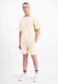 Lichtgele, gestructureerde polo met kraag, gecombineerd met bijpassende shorts. Bevat een subtiel logo en een relaxte pasvorm. Gestyled met witte sneakers.