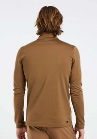 Brun långärmad skjorta med hög krage. Tillverkad av mjukt tyg, har en figursydd silhuett och en liten logotypdekoration nära fållen.