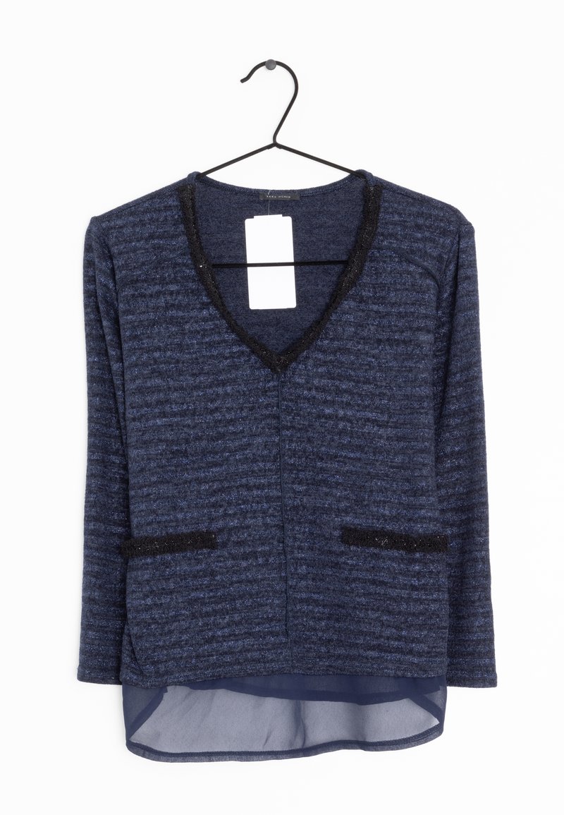 Pull en maille bleu marine à manches longues avec bordure noire au niveau du col en V et des poches, superposé à un tissu bleu marine translucide à l’ourlet, suspendu sur un cintre noir.