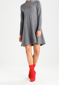 Robe grise à manches longues en tissu doux avec une jupe évasée, accompagnée de chaussettes rouges vives aux chevilles pour un contraste.