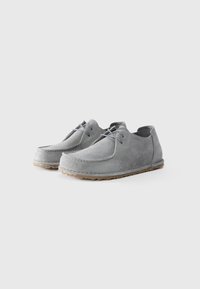 Chaussures en suède gris avec un bout arrondi et un laçage. Caractéristiques d'une tige texturée et d'une semelle en caoutchouc avec un motif de traction.