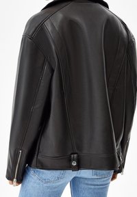 Giacca di pelle nera con una texture liscia, vestibilità oversize, cuciture cambiate e polsini con zip. Presenta una chiusura a scatto all'orlo.