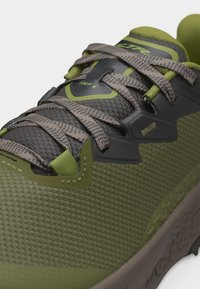 Κοντινό πλάνο πεζοπορικού παπουτσιού σε ελιάς πράσινο και γκρι, με υφασμάτινη υφή, δεσίματα διασταυρωτά και ενισχυμένες τρύπες για κορδόνια.