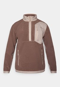 Veste pull brun avec un col montant, une fermeture éclair à l'avant et une poche poitrine en biais. Présente des accents beiges et des poches latérales zippées. Texture douce.