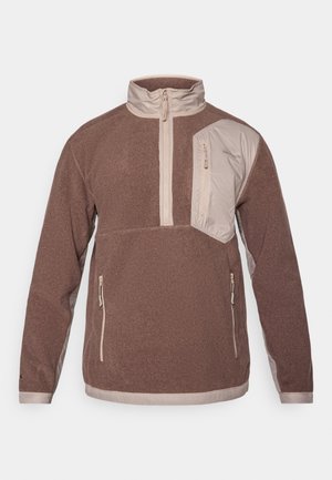 Brown pullover jacket with a high collar, front zipper, and an angled chest pocket. Features beige accents and side zip pockets. Soft texture.