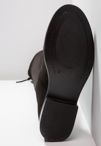 Bottine en suède noir avec un embout arrondi et une semelle en caoutchouc texturé. Caractéristiques : un petit talon carré et une fermeture à lacets. Taille 37 indiquée sur la semelle.