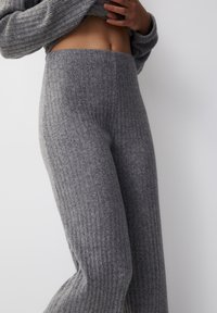 Grijze geribbelde gebreide broek met een hoge taille. De textuur is zacht en rekbaar, met verticale lijnen over de stof.