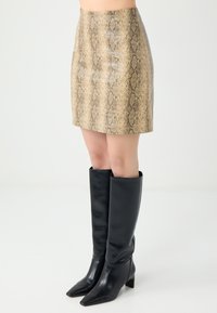 Mini-jurk met slangenhuidpatroon in beige met een gladde textuur. Gecombineerd met knielange zwarte leren laarzen met een spitse neus en blokhak.