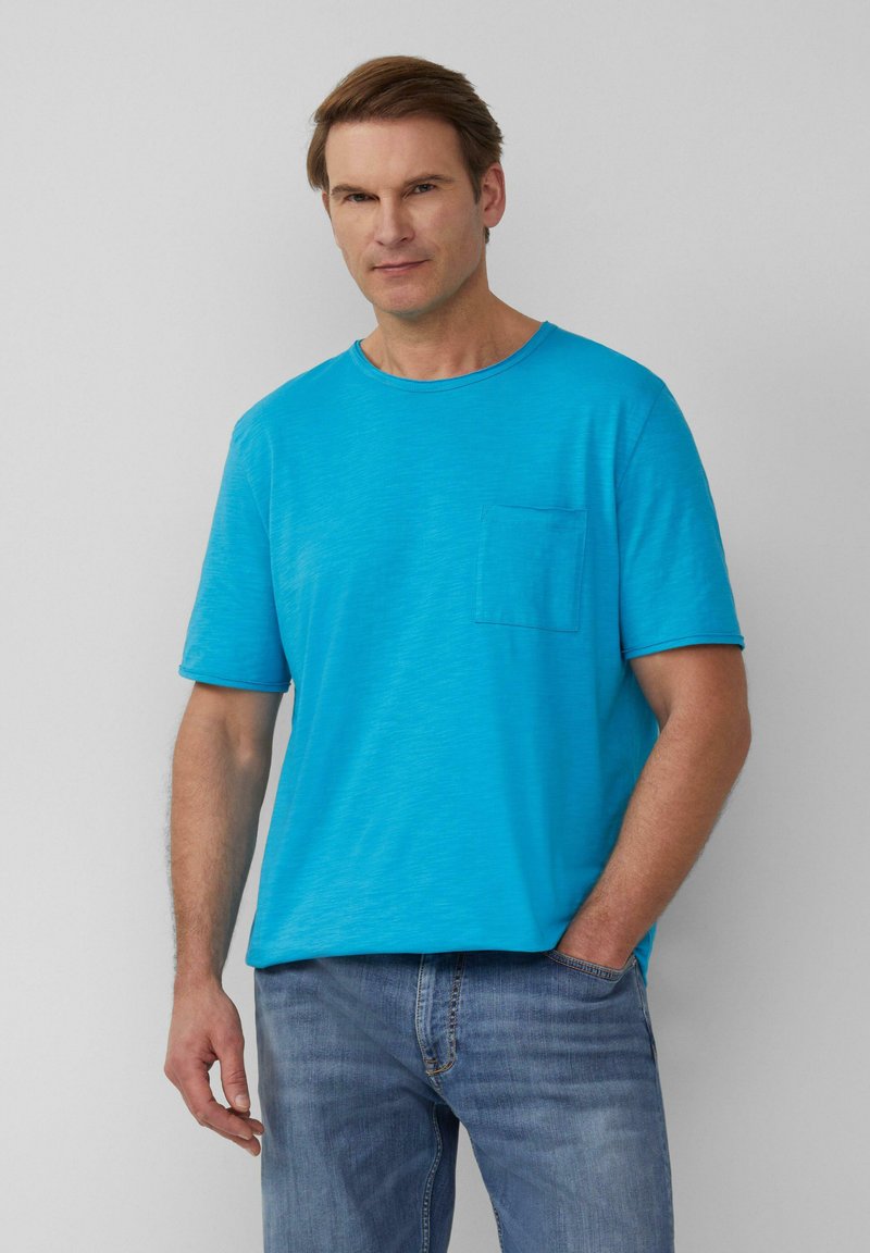 Turquoise T-shirt met korte mouwen van zachte stof, met een ronde halslijn en een voorvak. Gepaard met lichtblauwe jeans.