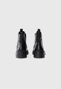 Botas de tobillo de cuero negro con puntera redonda, lados texturizados y suela de plataforma elevada. Cuenta con un cierre de cremallera y tiradores de tela.