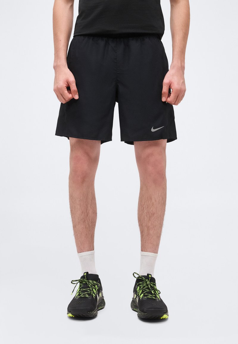 Άνδρας που φοράει μαύρα αθλητικά σορτς με το λογότυπο της Nike, άσπρες κάλτσες και μαύρα παπούτσια τρεξίματος με φωσφοριζέ πράσινα κορδόνια και λεπτομέρειες.